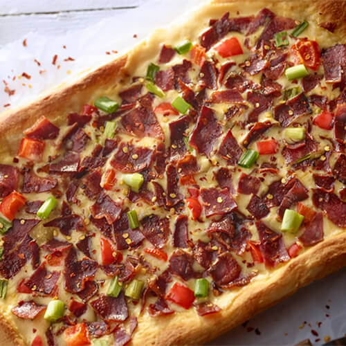 A rectangular flatbread pizza, topped with cheddar cheese, green onion, red bell pepper and JENNIE-O® turkey bacon.
