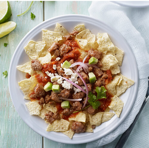 Turkey breakfast sausage chilaquiles on a white plate on a wood table.