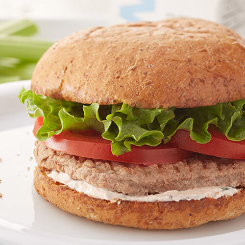 Lean turkey patties topped with lettuce, tomato, and a Sriracha garlic yogurt sauce, served on a white plate.