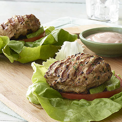 Turkey patty in lettuce wraps with creamy salsa on a wood plate.