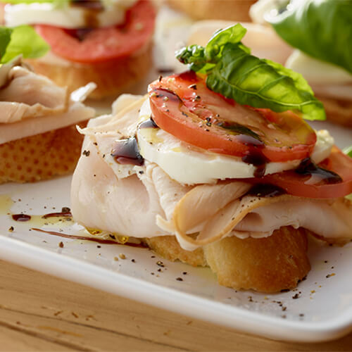 Turkey caprese bruschetta drizzled with balsamic vinegar on a white tray.