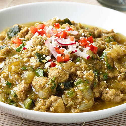 Turkey chili verde garnished with tomato and onion in a white bowl.