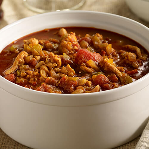 A hearty chili chock full of vegetables, spices, and ground turkey, served in a white bowl.