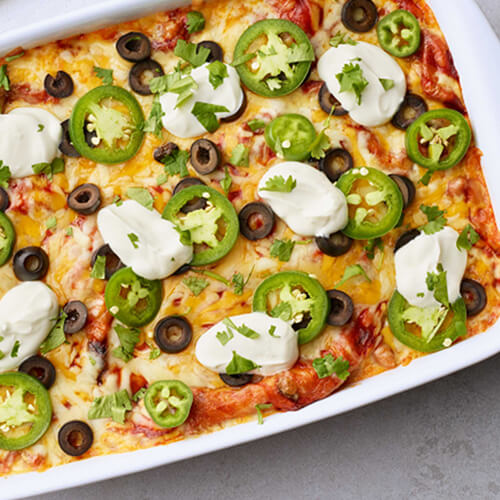 Turkey enchilada lasagna with jalapeno dolloped with sour cream in a white baking dish.