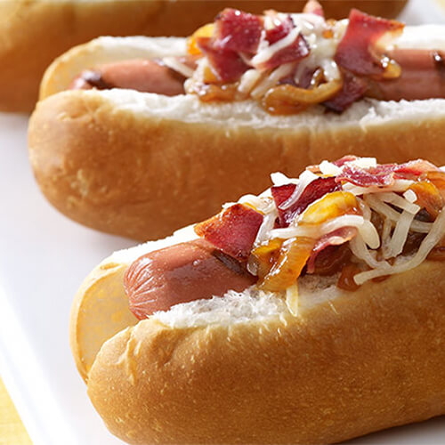 Juicy turkey franks topped with barbecue sauce, cheese, caramelized onions, and bacon, served on a white tray.