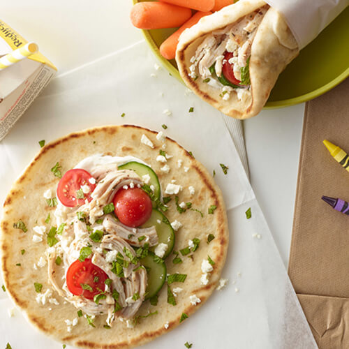 Turkey gyros sprinkled with cheese and a side of milk on a piece of parchment paper.