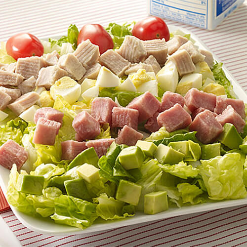 Rows of egg, turkey ham, ham, avocado, and cherry tomatoes, on a salad plate.