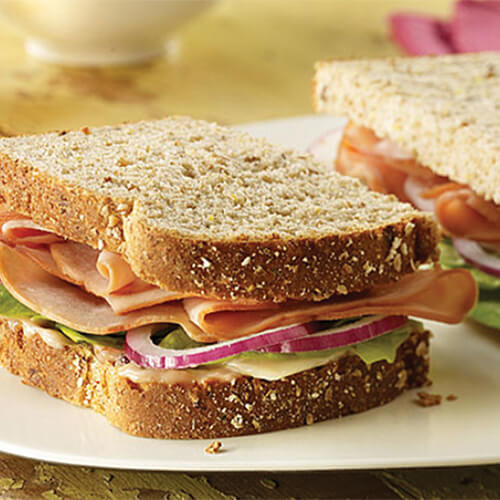 A rich cranberry mayo, red onion, vegetables, and Gouda cheese topped with roasted turkey, served on a white plate.