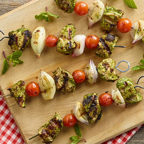 Skewered turkey, shallots, and tomatoes, in a tangy mint basil yogurt marinade on a wooden board.