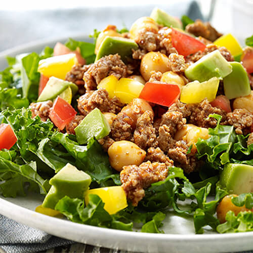 A turkey taco salad made with kale and salsa, served in a white plate atop a gray cloth.