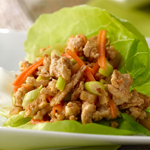 Lettuce wraps filled with a hearty portion of turkey, carrots, and green onion, served in a white bowl.