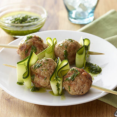 Turkey meatballs and zucchini ribbon skewers with a side of sauce on a white plate.