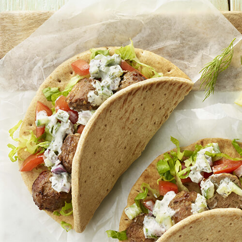 A Mediterranean-style gyro filled with turkey meatballs, lettuce, tomato, and tzatziki in a folded pita served on parchment paper on a wooden board.