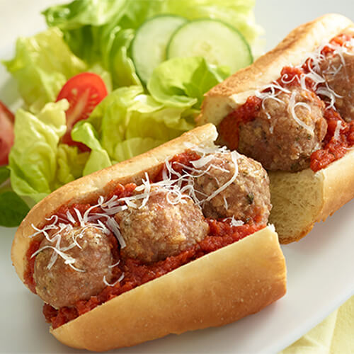 A hearty amount of turkey meatballs, parmesan cheese, and swimming with pasta sauce, served on a submarine roll on a white plate, garnished with a salad.