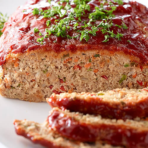 A juicy flavorful hunk of turkey meatloaf, topped with a barbecue-style glaze and parsley, served with a herb sprig, on a white plate.