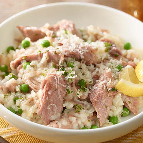 A hearty portion of risotto, peas, chopped turkey and parmesan, served in a white plate on a yellow colored napkin.