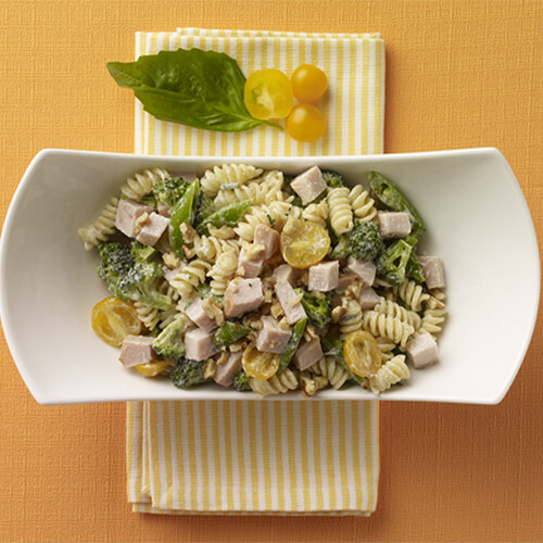 Spiral pasta tossed with JENNIE-O® Turkey, spinach, yellow tomatoes, and broccoli in a white plate on a yellow background.