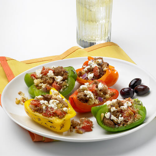 Colorful bell peppers filled with goat cheese, couscous vegetables and lean ground turkey on a white plate, in on an orange napkin and a white background.