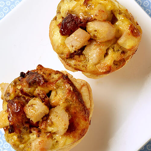 Flaky cups of turkey, basil pesto, parmesan cheese and sun-dried tomato on a white plate on a light blue and white tablecloth.