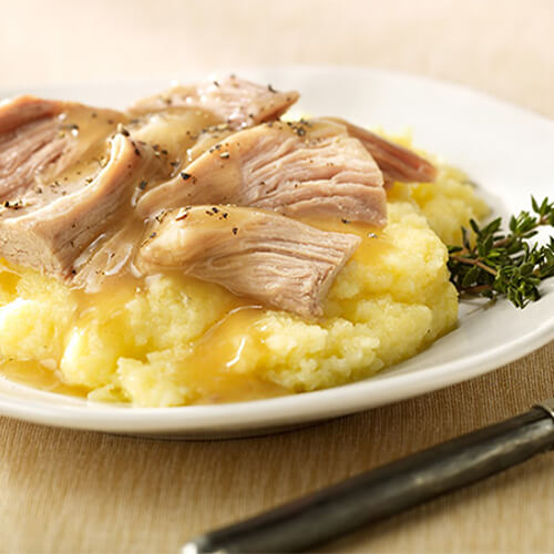 A generous portion of roast turkey, soft mashed potatoes, polenta, and gravy, on a white plate, served with sprigs of rosemary.