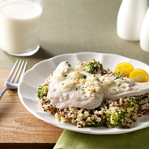 A large portion of Quinoa packed with veggies, topped with a savory, creamy, sauce, served on a white plate atop a green cloth.