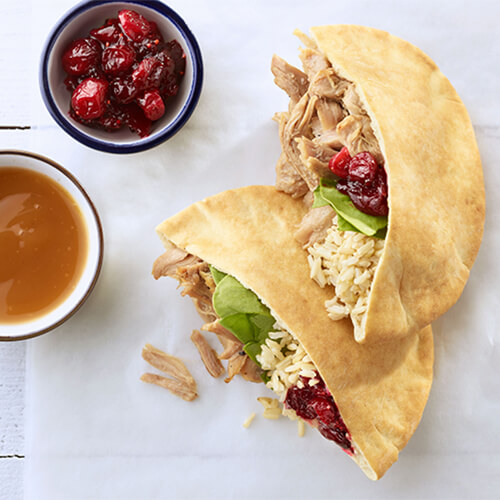 Turkey rice and cranberry pitas with a side of cranberries on a white tabletop.