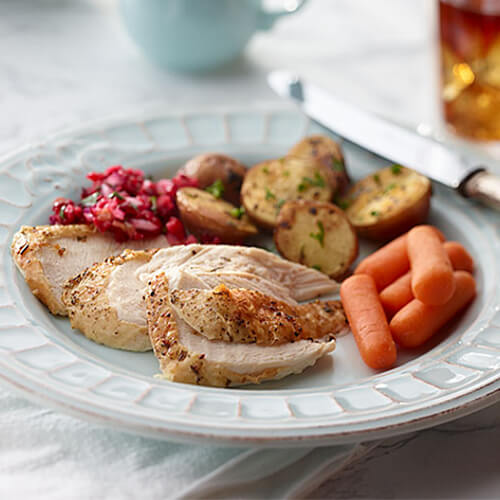 A hearty portion of roasted turkey, served with steamed carrots, a cranberry relish, and a herbed potatoes, served on a painted plate.