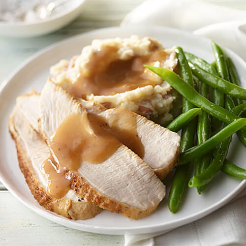 A generous portion of roast turkey, soft mashed potatoes, gravy, and tender green beans, on a white plate.