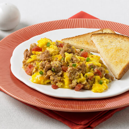 A hearty portion of of ground turkey and scrambled eggs, made with green onions and fresh salsa, served with buttered toast on a white plate served on a red plate and napkin.