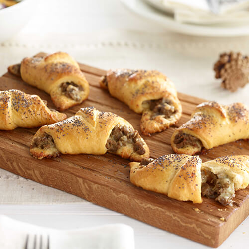 Turkey sausage and cheese crescent rolls arranged on a wood plate on a white table.