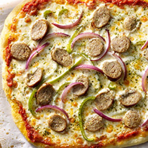 A hearty pizza topped with red onion, bell pepper, cheese and marinara sauce, all buttoned up with Italian turkey sausage, laid on parchment paper and a wooden pizza board.