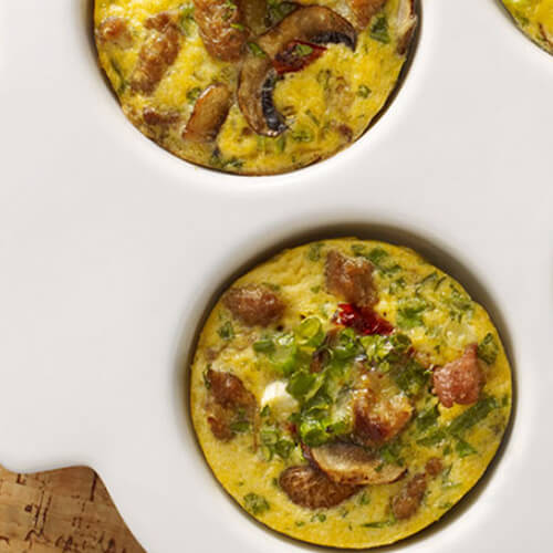 Mini quiches packed with veggies, cheese and turkey, served in a white muffin tin on a wooden table.
