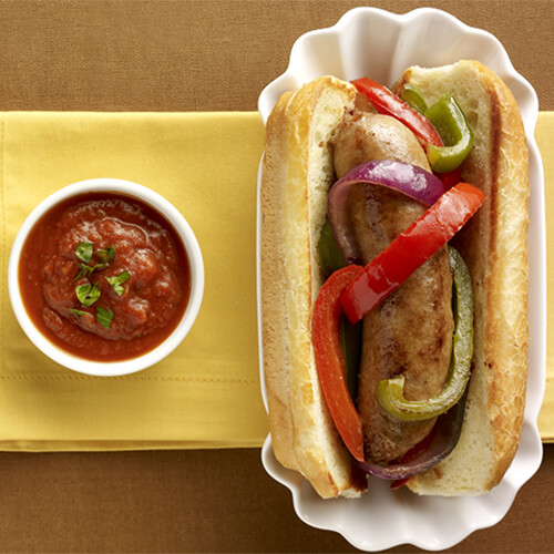 A hoagie made with sweet Italian turkey sausage, topped with sautéed peppers and onions and served with a side of marinara on a yellow napkin with a linen background.