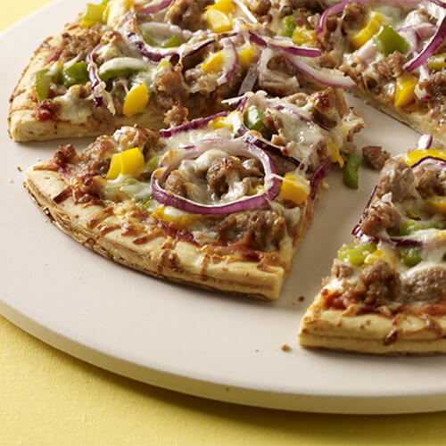 Thin crust pizza with turkey sausage, yellow bell peppers, onions, and cheese, placed on a white plate.