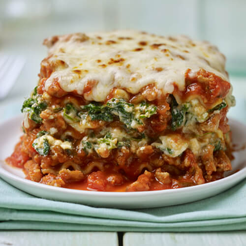 A meaty hunk of a spinach and ground turkey lasagna on a small white plate.