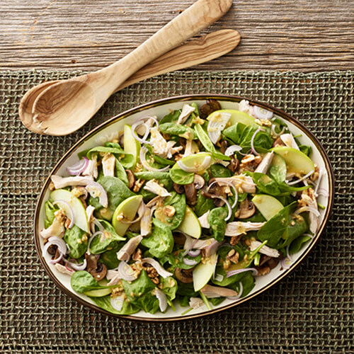 Turkey spinach mushroom salad with walnut vinaigrette in a grey bowl on a wood table.