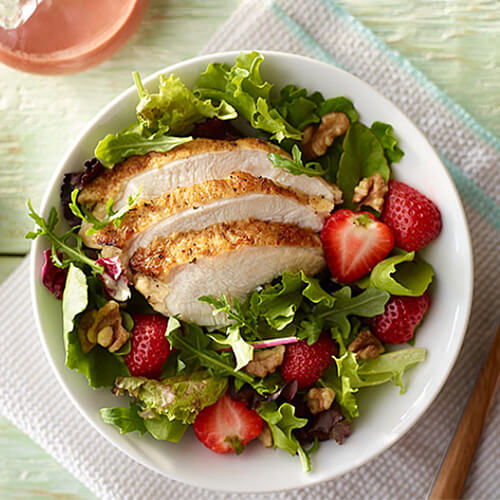 Fresh berries, walnuts, and juicy hunks of turkey served in a white bowl on a gray napkin.