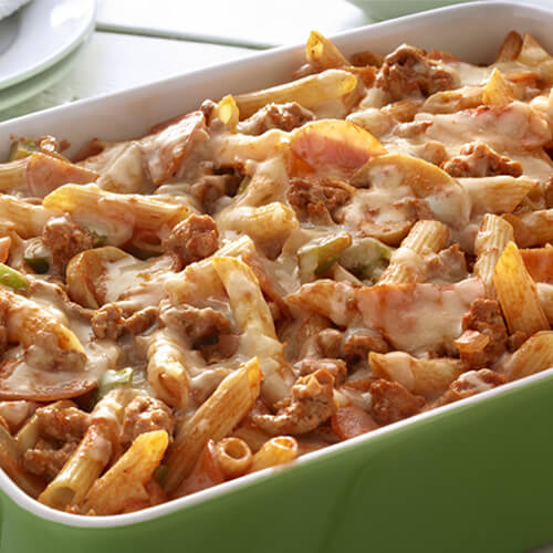 A casserole made out of penne pasta, ground turkey, Canadian bacon, mushrooms, vegetables, and pizza sauce, in a green casserole tray on a wooden table.