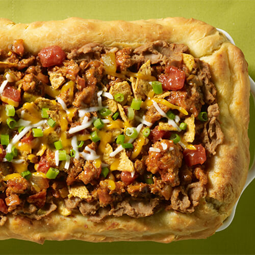 A deep-dish cornbread crusted pie filled with a variety of flavor from fresh green pepper, salsa, shredded cheese and lean ground turkey in a white casserole tray, atop a green tablecloth.
