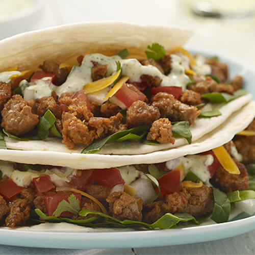 2 delicious tacos filled with spinach, cheese, pico de gallo, seasoned turkey and cilantro lime sauce, served in a blue plate.