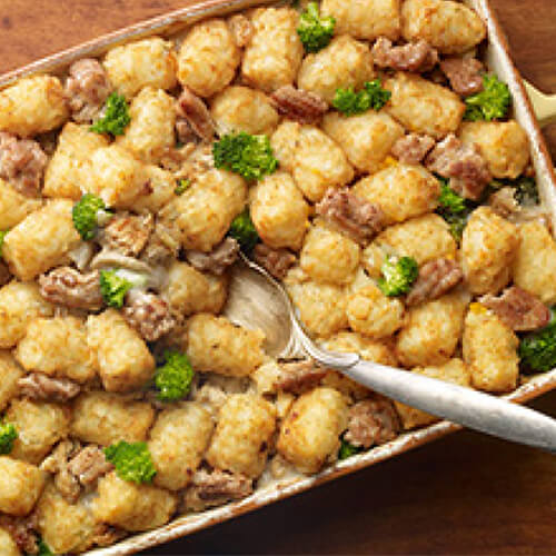 A creamy casserole, filled with tater tots, broccoli, and ground turkey, served in a green casserole pan atop a wooden table.