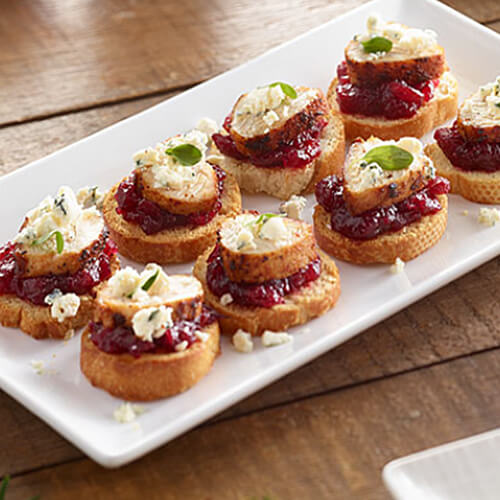 Turkey tenderloin crostini sprinkled with cheese arranged on a white plate.