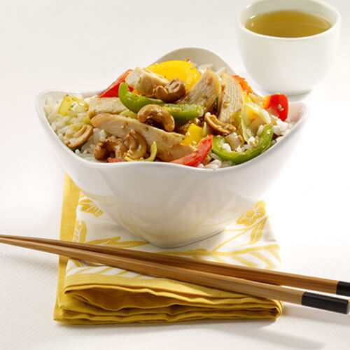 A hearty bowl of turkey, and vegetables served over rice on a yellow napkin with chopsticks, with a white background.