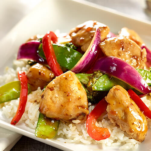 An enormous pile of veggies and turkey strips, served on a bed of rice on a white plate.