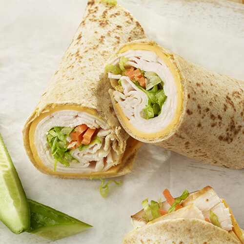 A wrap stuffed with with cheese, turkey, lettuce, carrot, and a Dijon mayo, served on parchment paper.