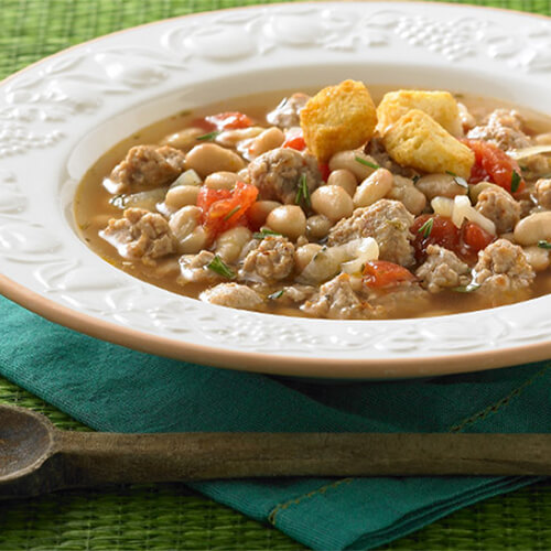 White bowl of JENNIE-O® Turkey with tuscan beans and tomatoes on a green napkin.