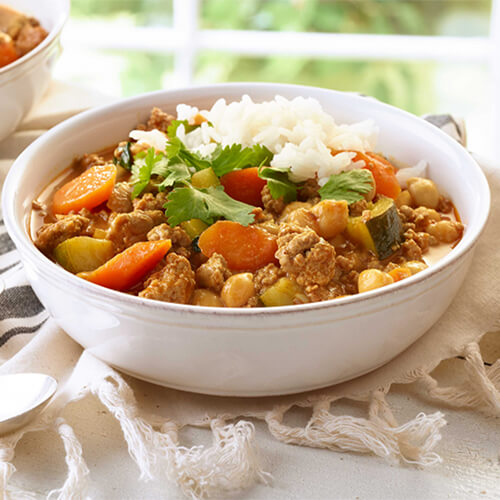 Turkey vegetable curry in a white bowl on a white table.