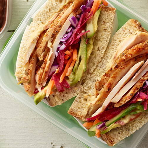 Turkey vegetable sandwich on a green plate on a white wood table.