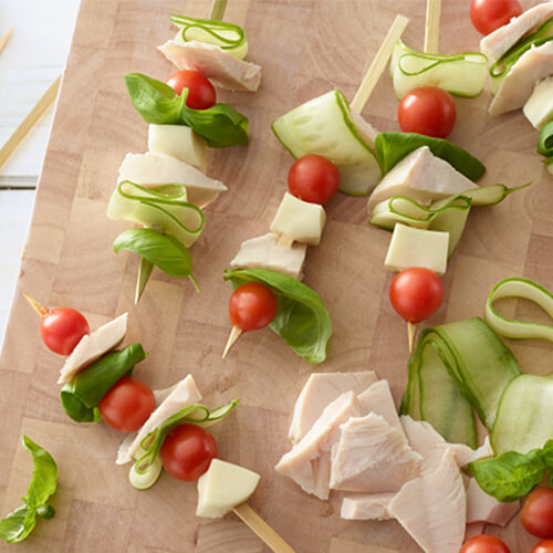 Skewered turkey, cherry tomatoes, mozzarella cheese, and basil, on top of a wooden board.