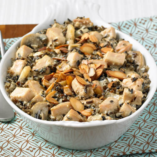 Sautéed mushrooms, roasted turkey, wild rice, and water chestnuts served in a casserole style, in a white bowl atop a blue patterned cloth.